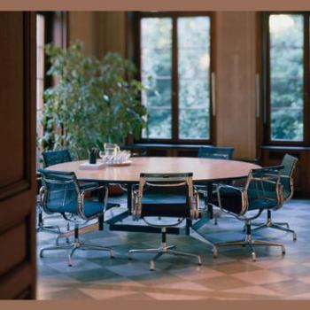 A round wooden table surrounded by 7 black chairs 